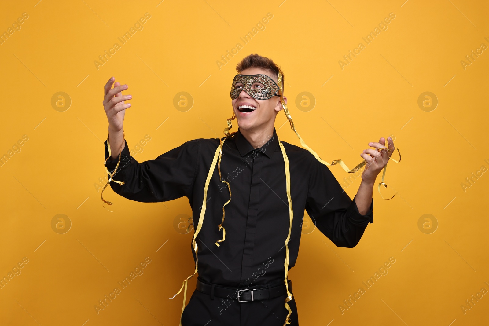 Photo of Charming young man wearing carnival mask on orange background