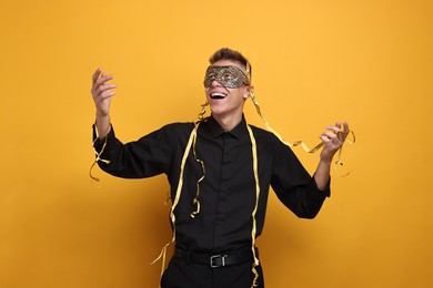 Charming young man wearing carnival mask on orange background