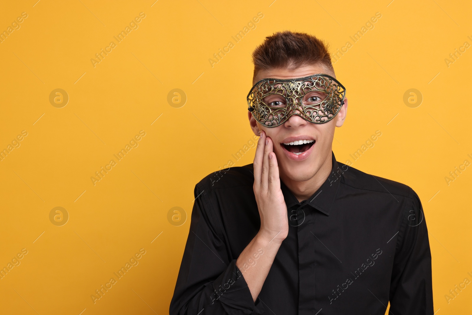 Photo of Charming young man wearing carnival mask on orange background. Space for text