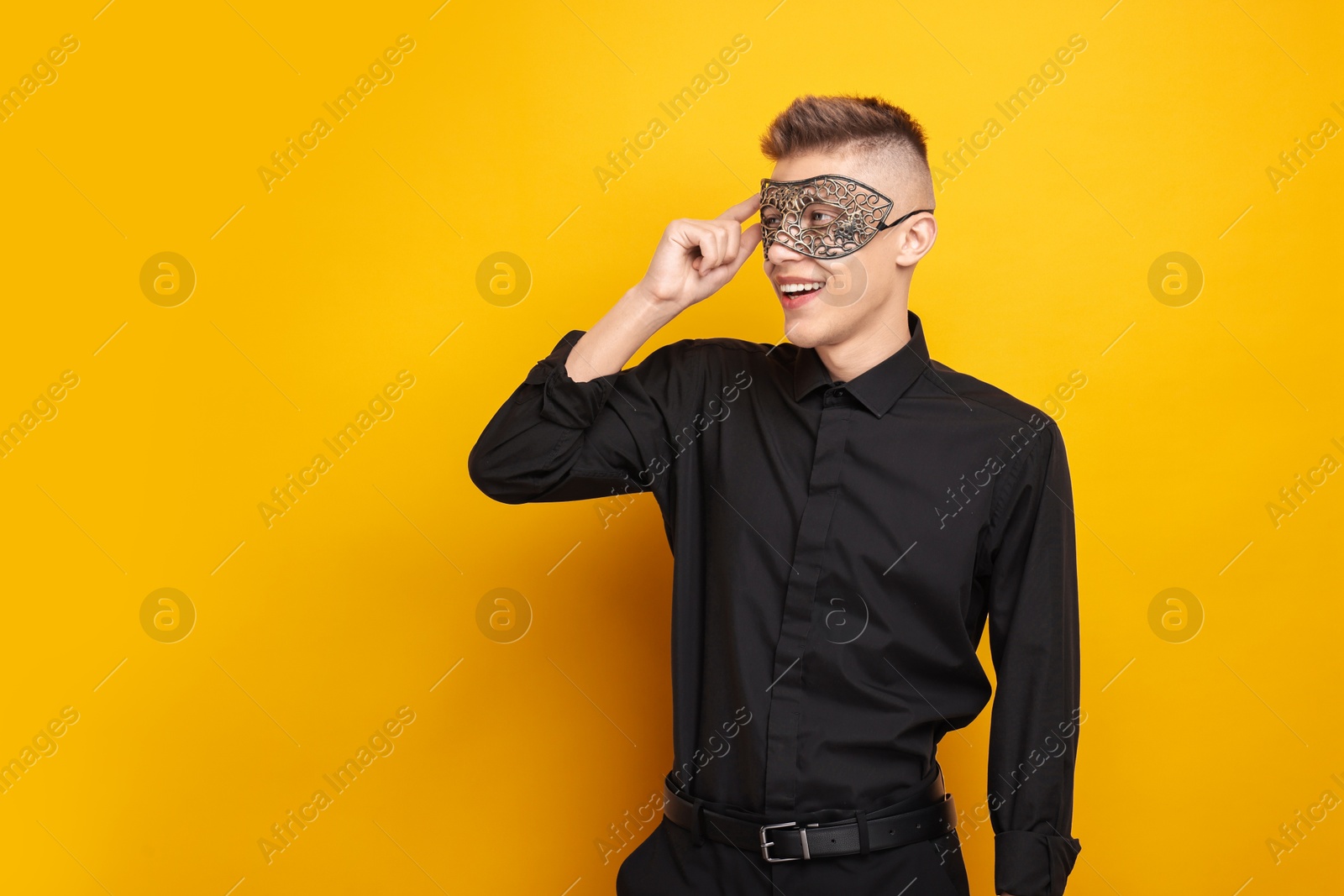 Photo of Charming young man wearing carnival mask on orange background. Space for text