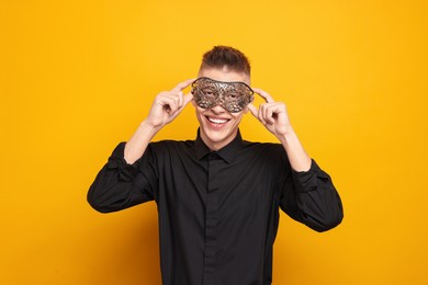 Charming young man wearing carnival mask on orange background