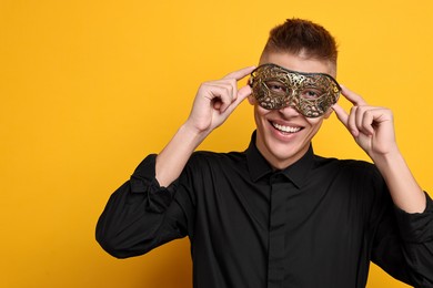 Charming young man wearing carnival mask on orange background. Space for text