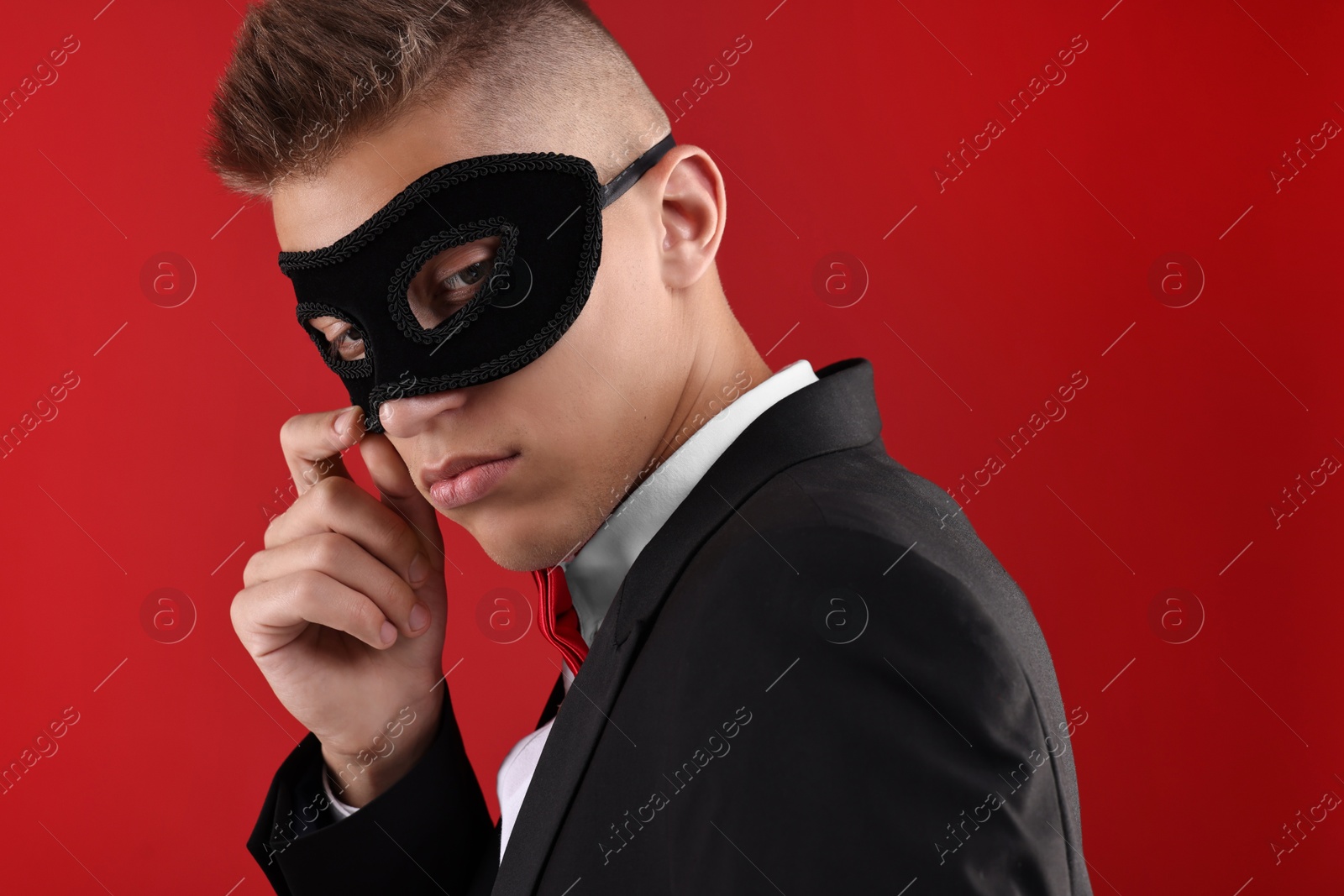 Photo of Charming young man wearing carnival mask on red background