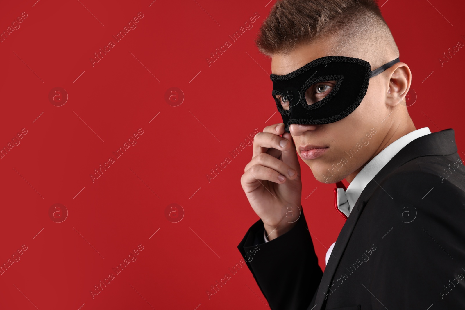 Photo of Charming young man wearing carnival mask on red background. Space for text