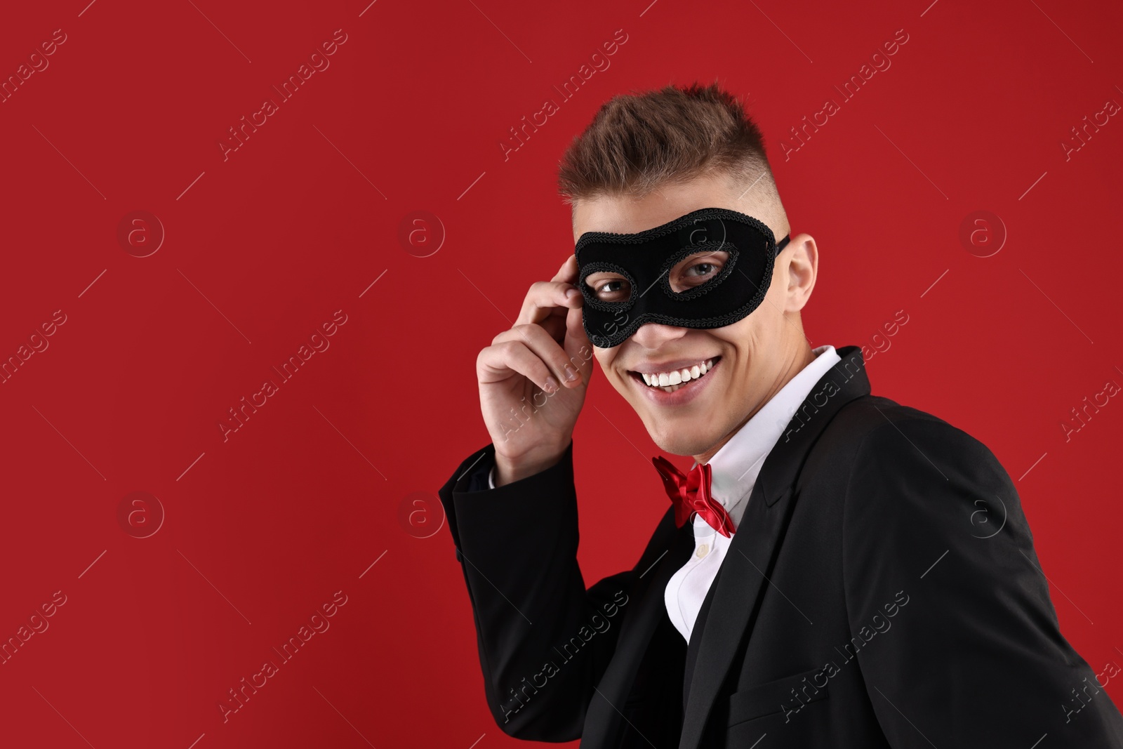 Photo of Charming young man wearing carnival mask on red background. Space for text