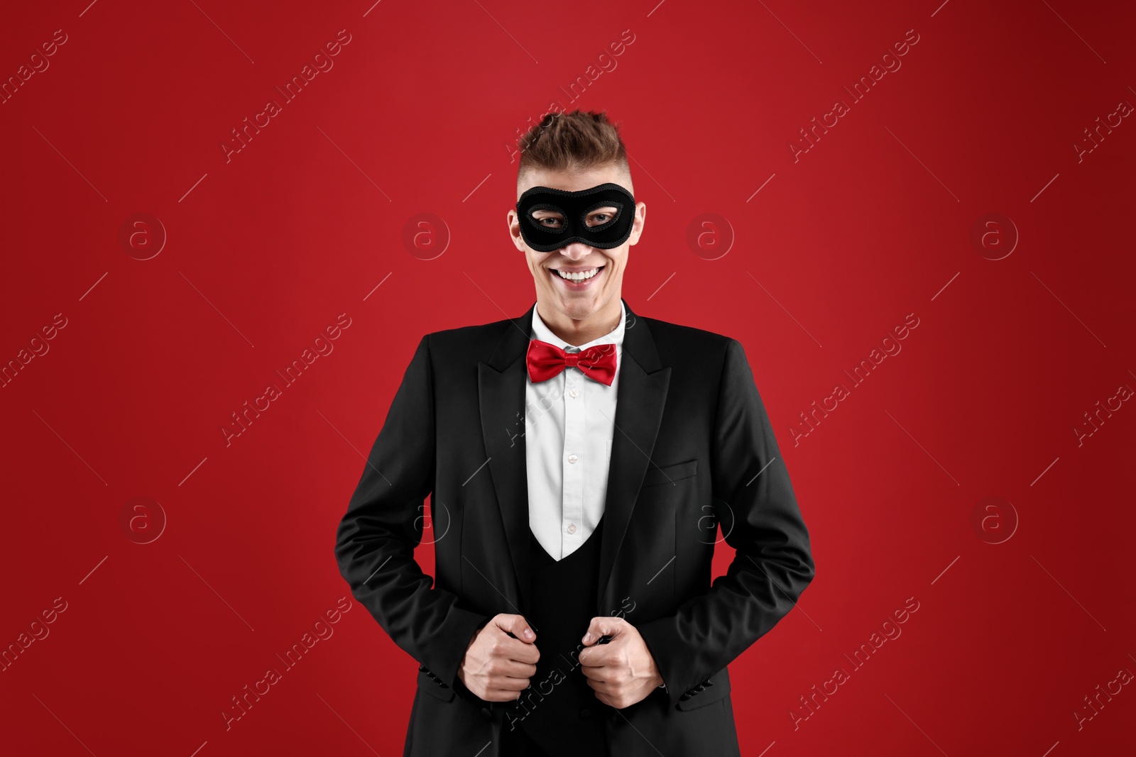 Photo of Charming young man wearing carnival mask on red background