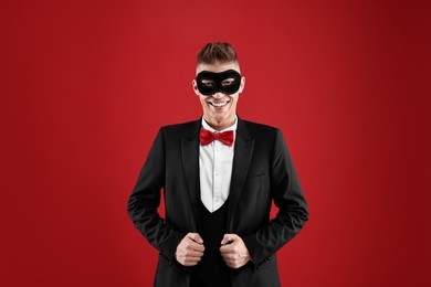 Charming young man wearing carnival mask on red background