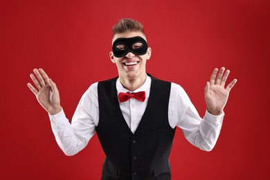 Photo of Charming young man wearing carnival mask on red background