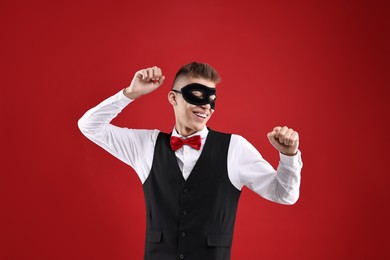 Photo of Charming young man wearing carnival mask on red background