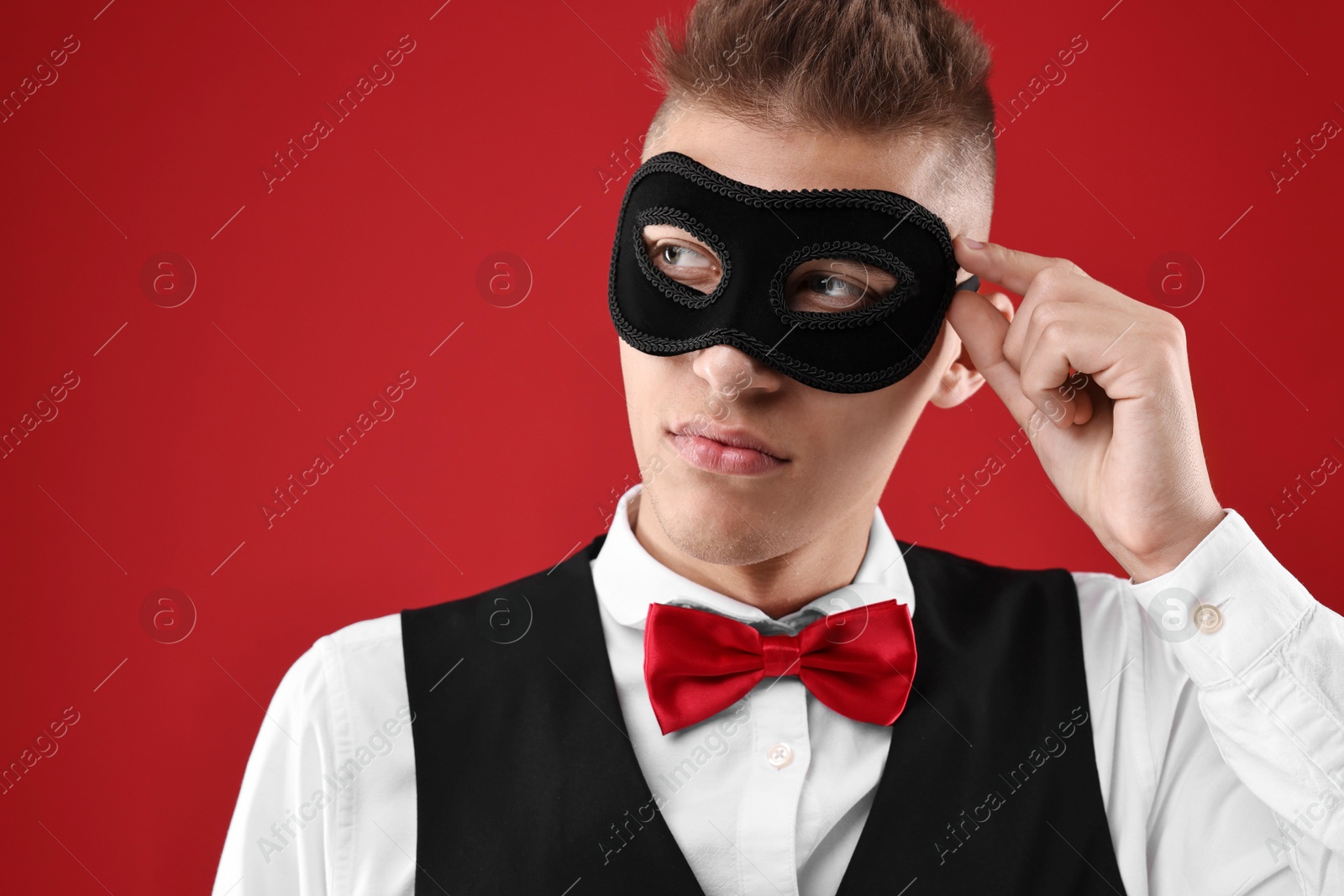 Photo of Charming young man wearing carnival mask on red background