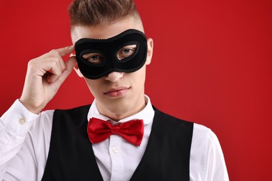 Photo of Charming young man wearing carnival mask on red background. Space for text