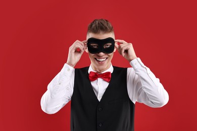 Photo of Charming young man wearing carnival mask on red background