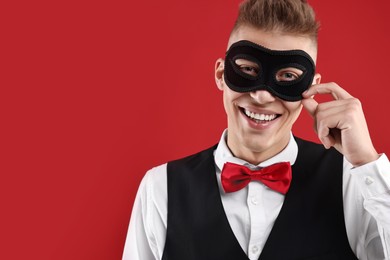 Photo of Charming young man wearing carnival mask on red background. Space for text