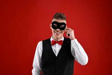 Photo of Charming young man wearing carnival mask on red background