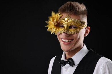 Charming young man wearing carnival mask on black background. Space for text