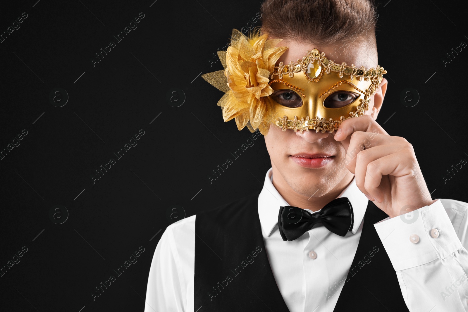 Photo of Charming young man wearing carnival mask on black background. Space for text