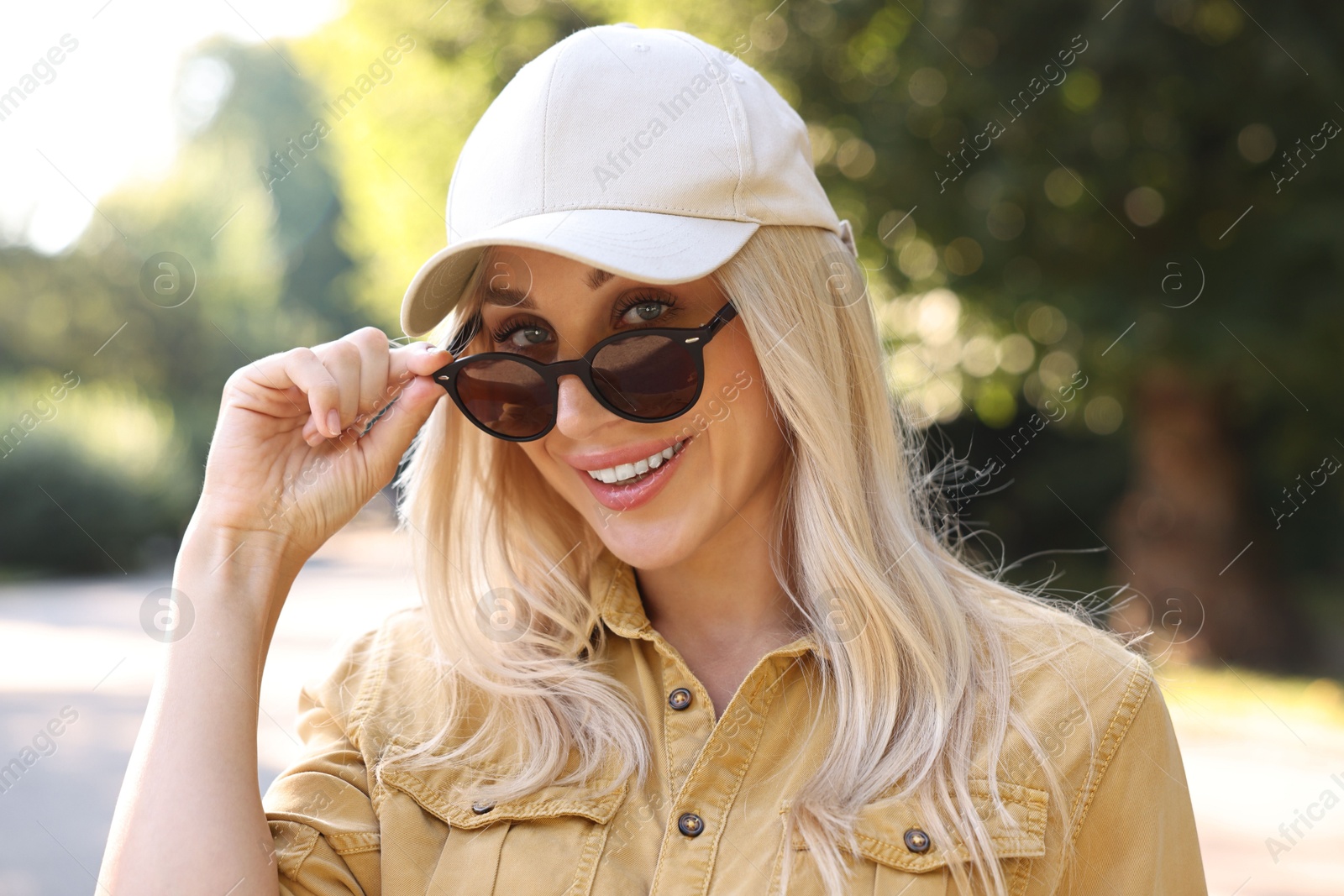 Photo of Portrait of smiling woman in baseball cap and sunglasses outdoors