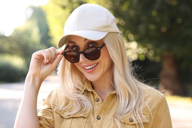 Portrait of smiling woman in baseball cap and sunglasses outdoors