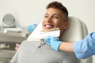 Photo of Doctor checking young man's teeth color in clinic, closeup. Dental veneers