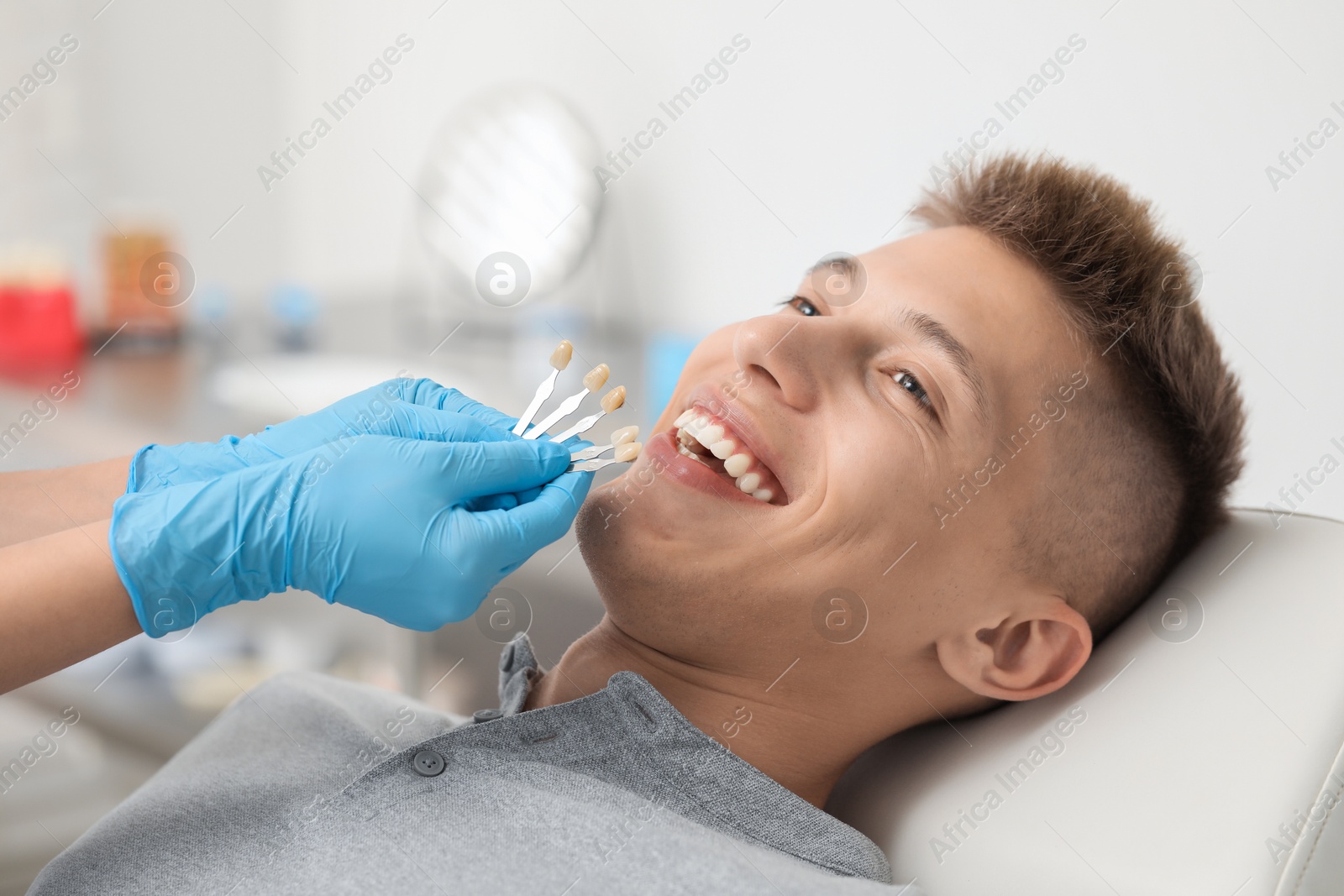 Photo of Doctor checking young man's teeth color in clinic, closeup. Dental veneers