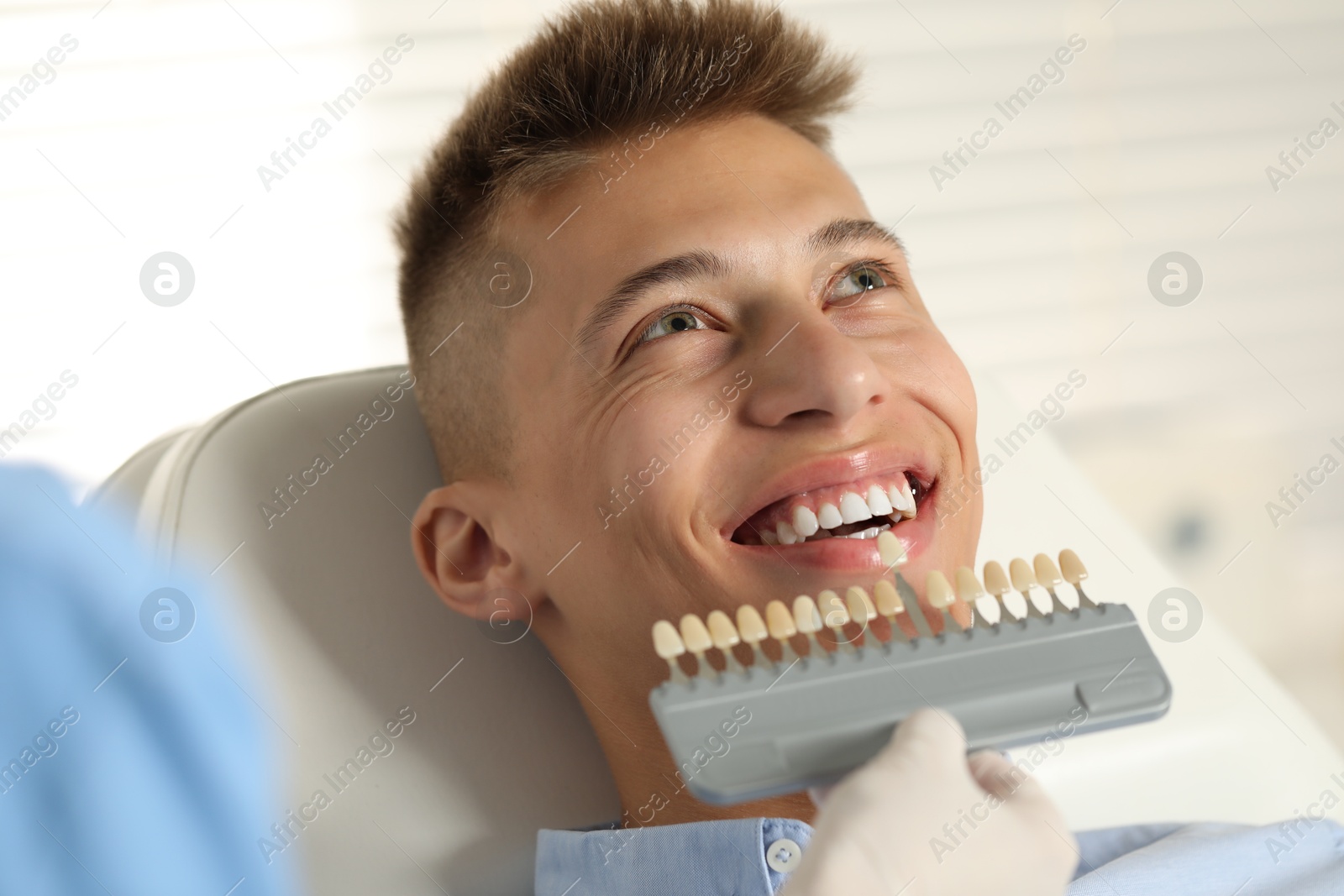 Photo of Doctor checking young man's teeth color in clinic, closeup. Dental veneers