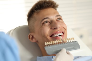 Doctor checking young man's teeth color in clinic, closeup. Dental veneers