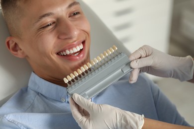 Doctor checking young man's teeth color in clinic, closeup. Dental veneers