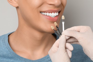 Doctor checking young man's teeth color on gray background, closeup. Dental veneers