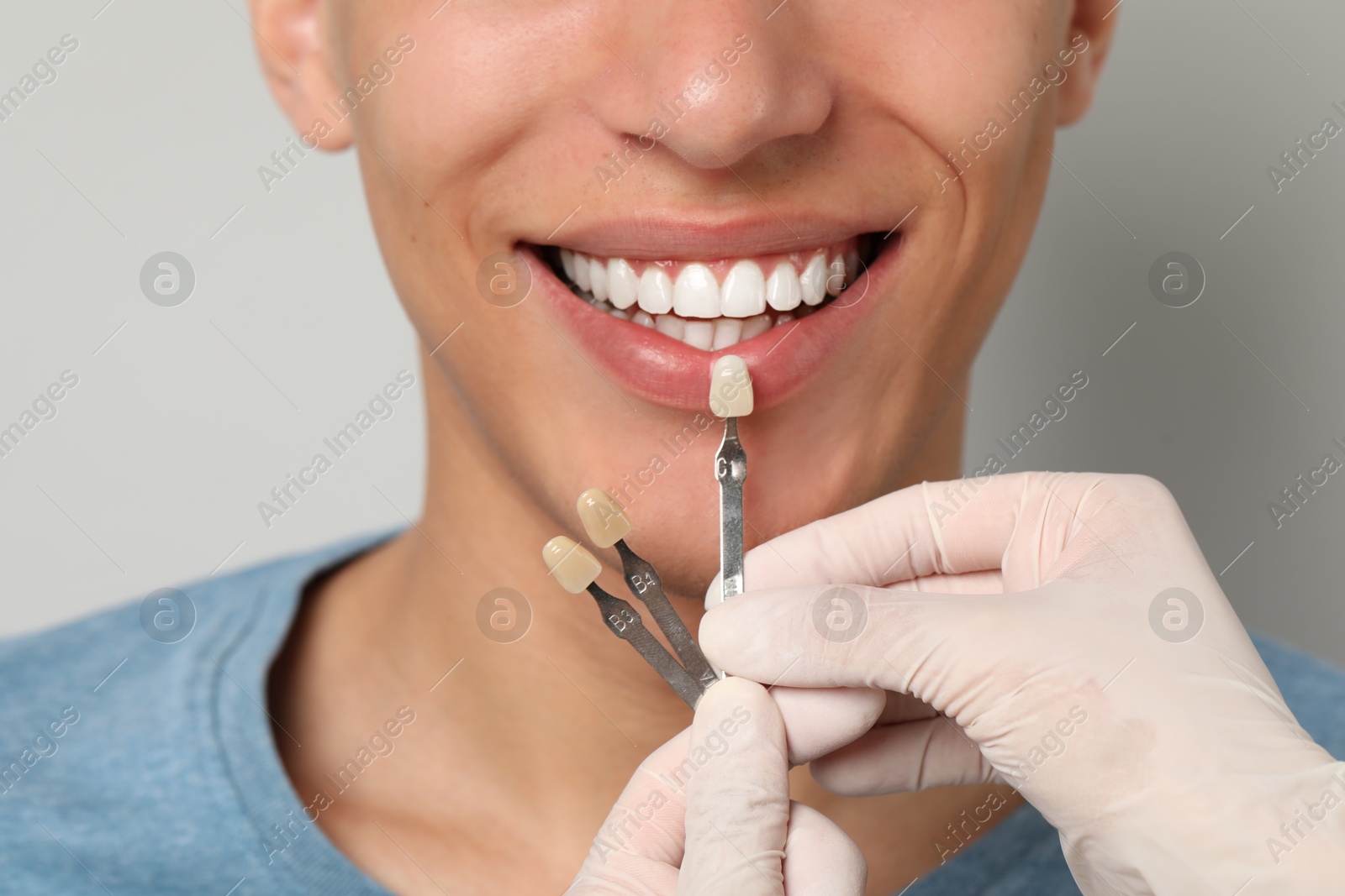 Photo of Doctor checking young man's teeth color on gray background, closeup. Dental veneers