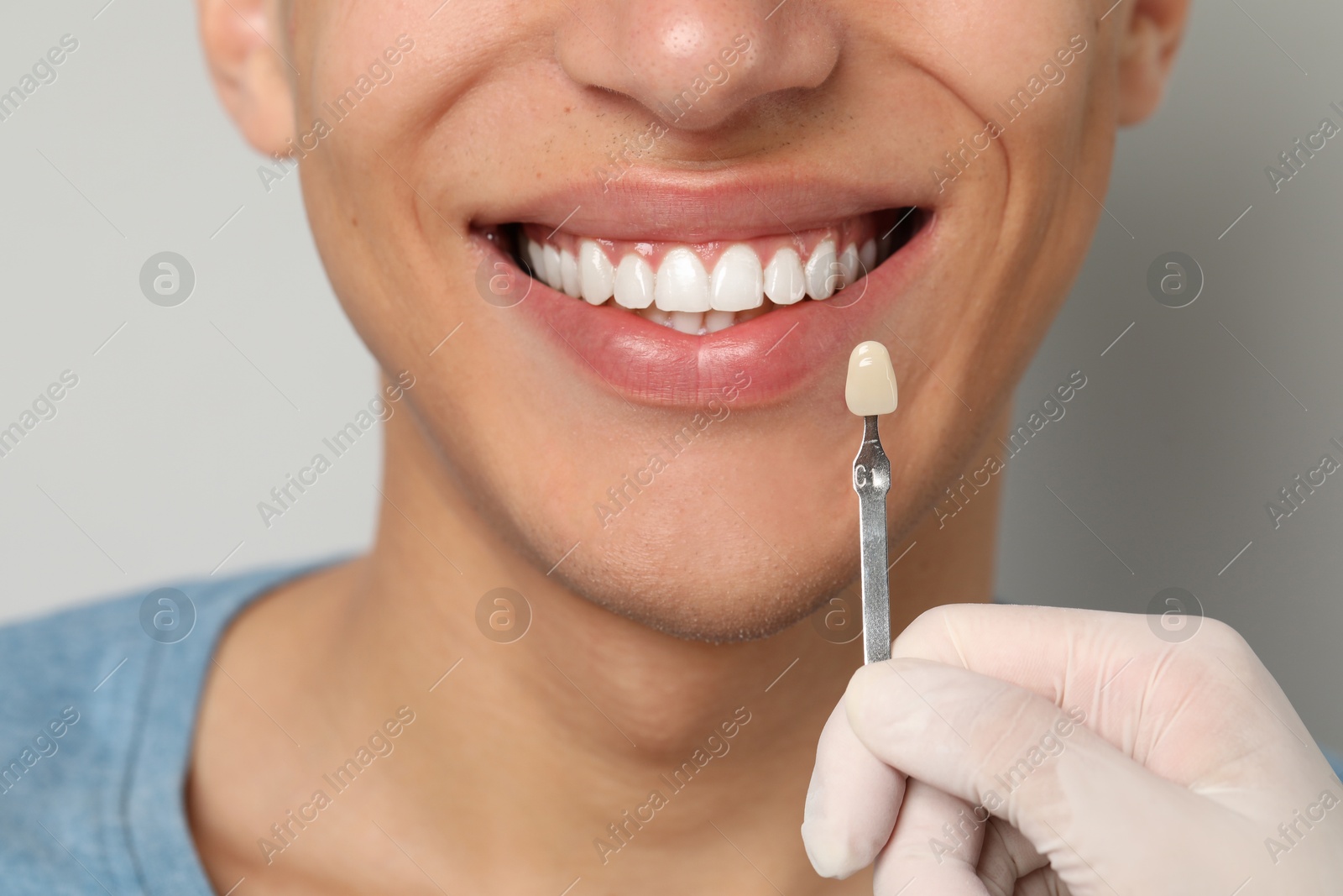 Photo of Doctor checking young man's teeth color on gray background, closeup. Dental veneers