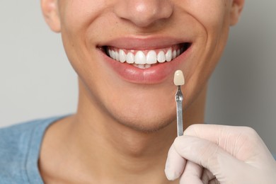 Doctor checking young man's teeth color on gray background, closeup. Dental veneers