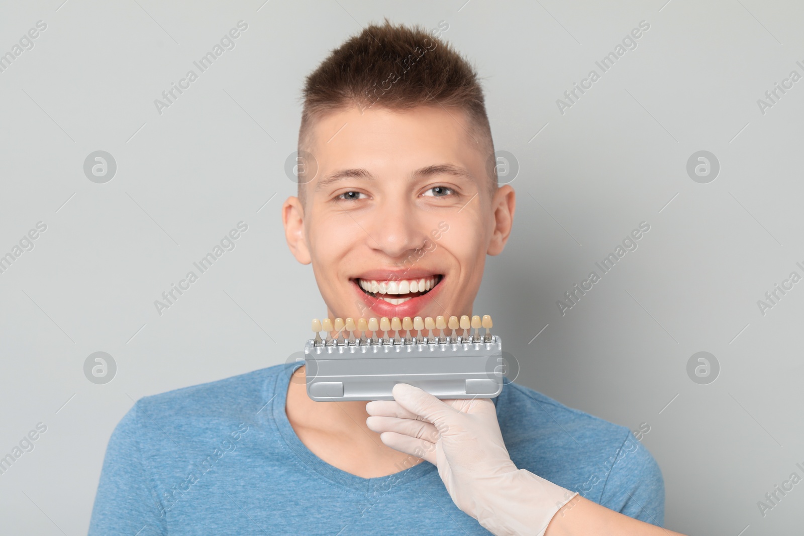 Photo of Doctor checking young man's teeth color on gray background, closeup. Dental veneers