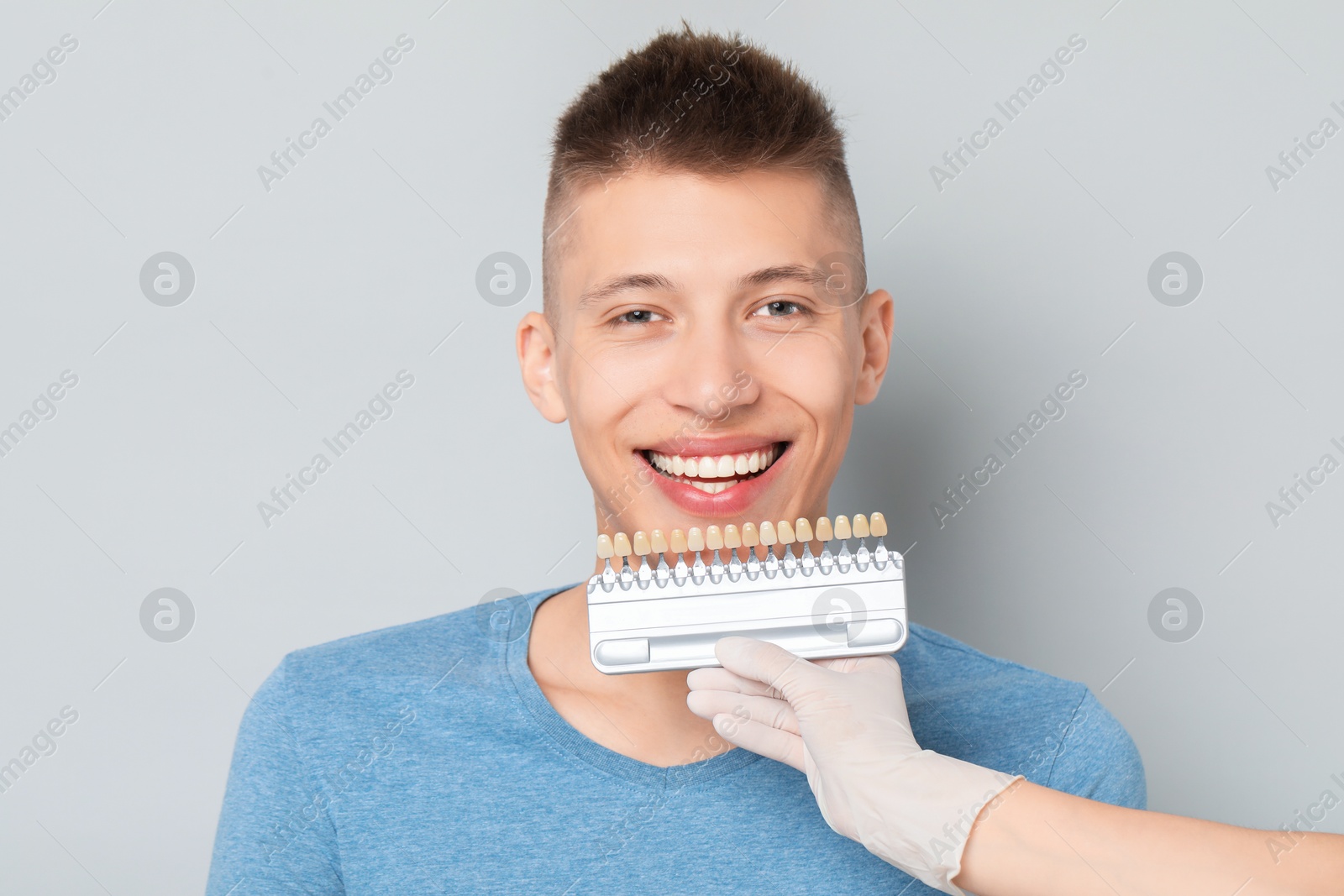 Photo of Doctor checking young man's teeth color on gray background, closeup. Dental veneers