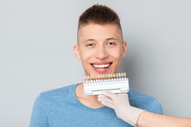 Doctor checking young man's teeth color on gray background, closeup. Dental veneers