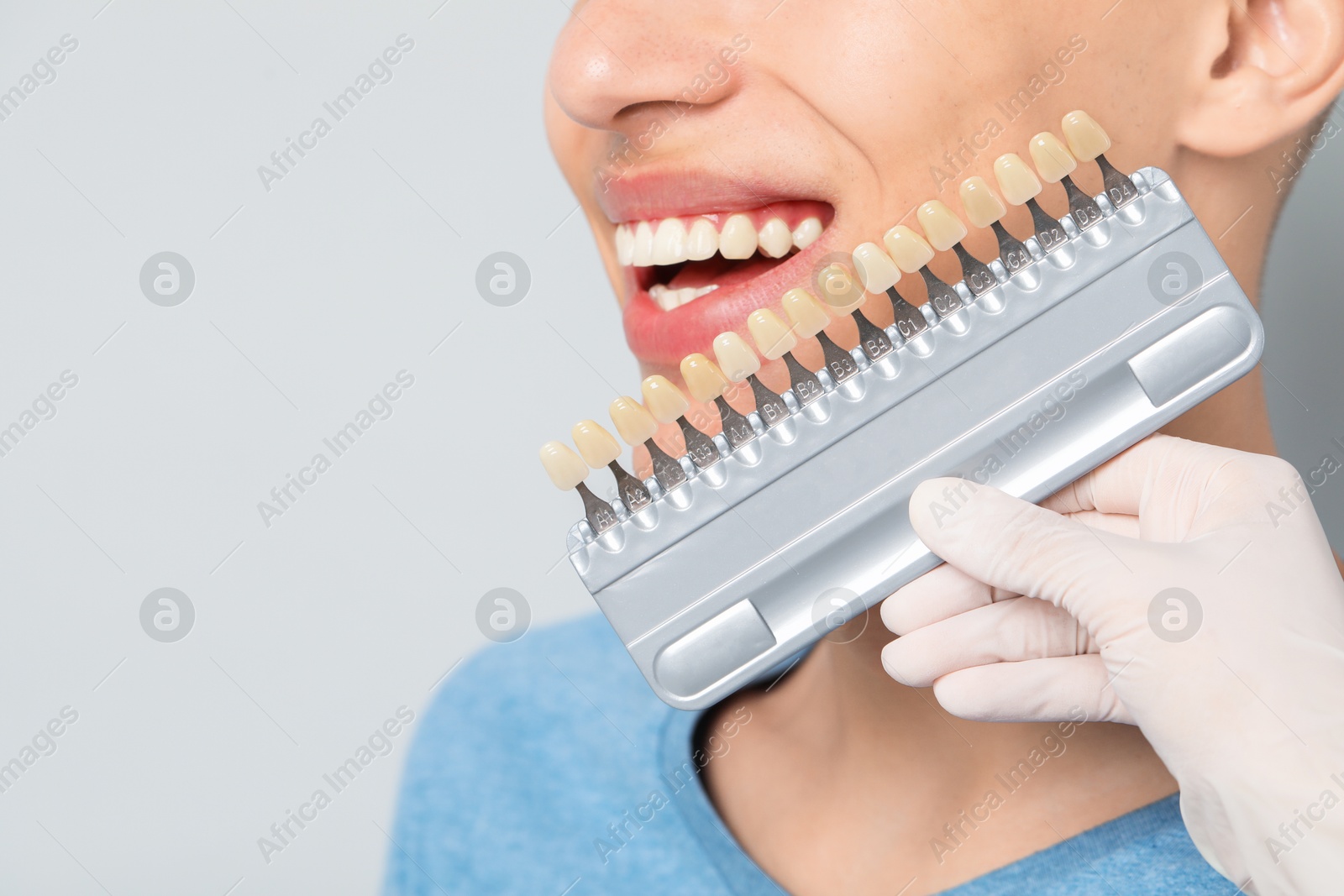 Photo of Doctor checking young man's teeth color on gray background, closeup with space for text. Dental veneers