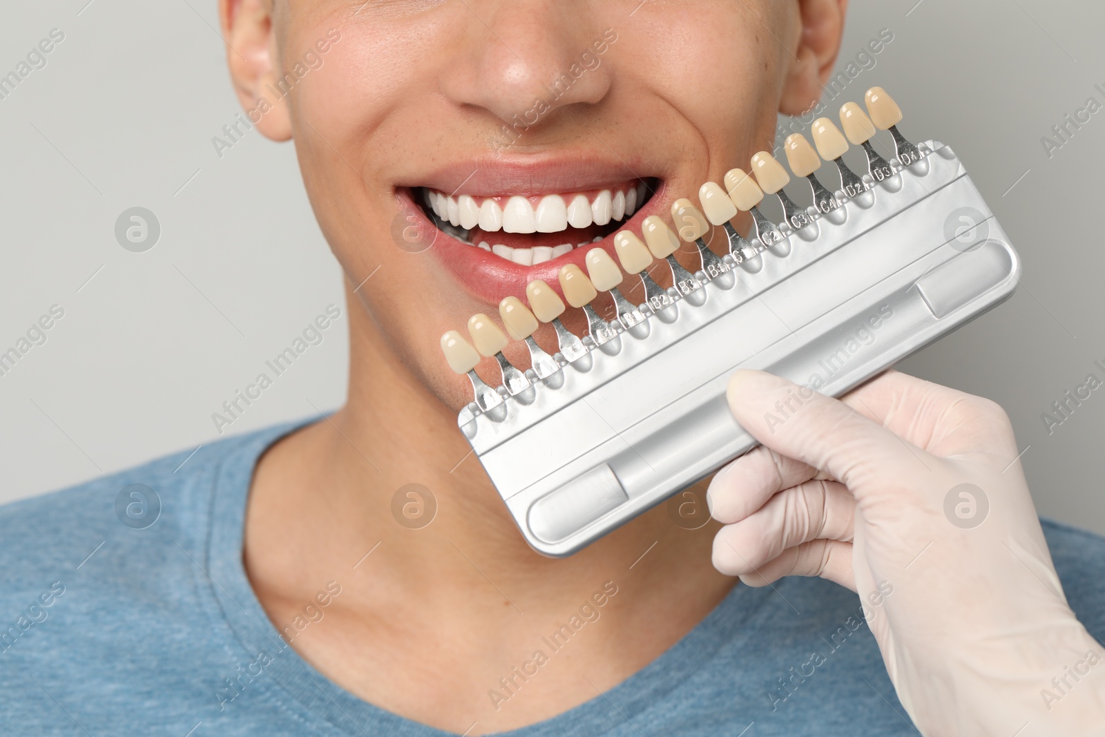 Photo of Doctor checking young man's teeth color on gray background, closeup. Dental veneers