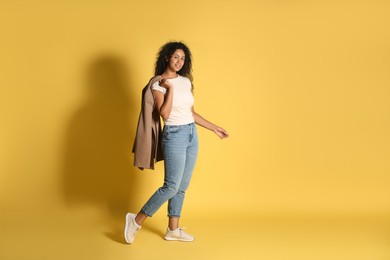 Beautiful woman with stylish jacket on yellow background