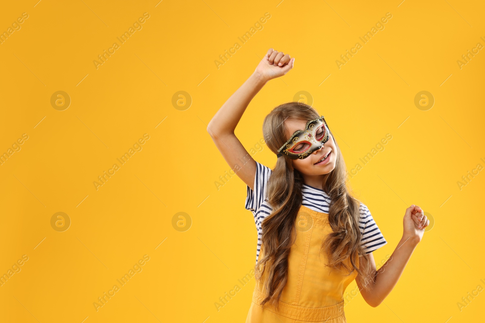 Photo of Cute girl wearing carnival mask on orange background, space for text