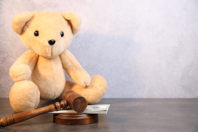 Photo of Alimony. Toy bear, wooden gavel and dollar banknotes on grey table, space for text