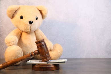 Photo of Alimony. Toy bear, wooden gavel and dollar banknotes on grey table, space for text