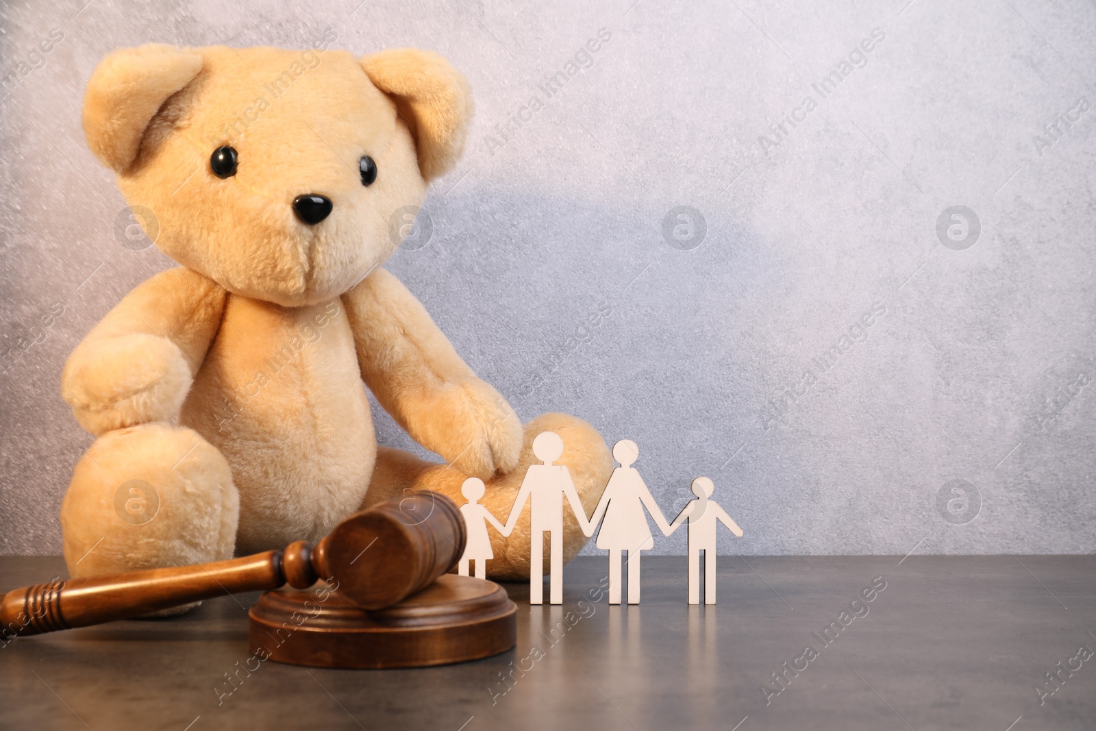 Photo of Alimony. Toy bear, wooden gavel and figures of family on grey table, space for text