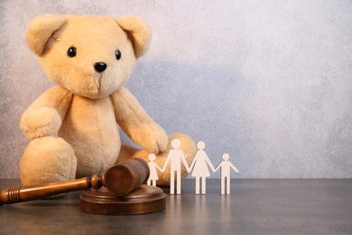 Photo of Alimony. Toy bear, wooden gavel and figures of family on grey table, space for text