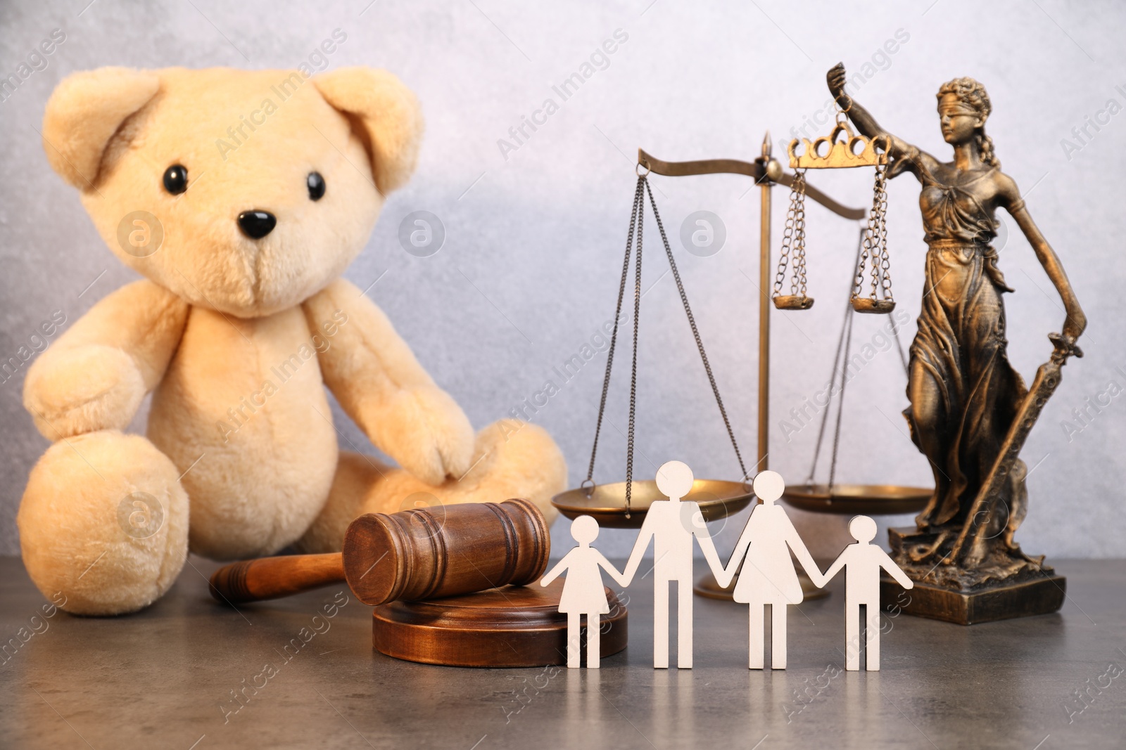 Photo of Alimony. Toy bear, wooden gavel, scales, figures of family and statue of Lady Justice on grey table