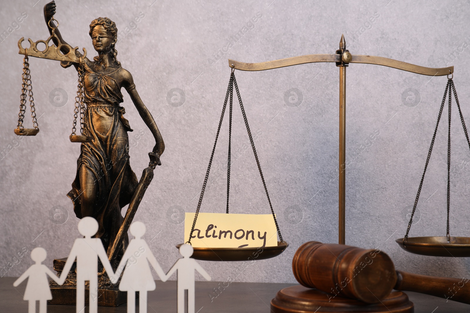 Photo of Card with word Alimony, wooden gavel, scales, figures of family and statue of Lady Justice on table