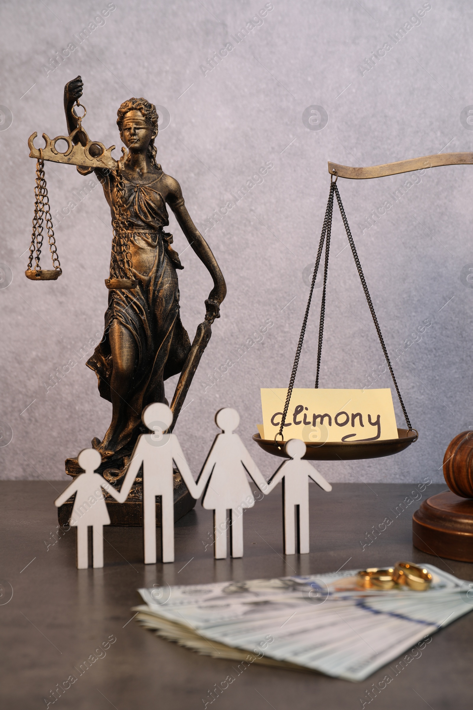 Photo of Card with word Alimony, figures of family, dollar banknotes, scales and statue of Lady Justice on grey table