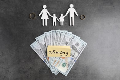 Card with word Alimony, dollar banknotes, wedding rings and figures of family on grey table, flat lay