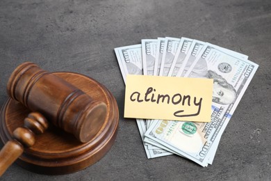 Photo of Card with word Alimony, dollar banknotes and wooden gavel on grey table