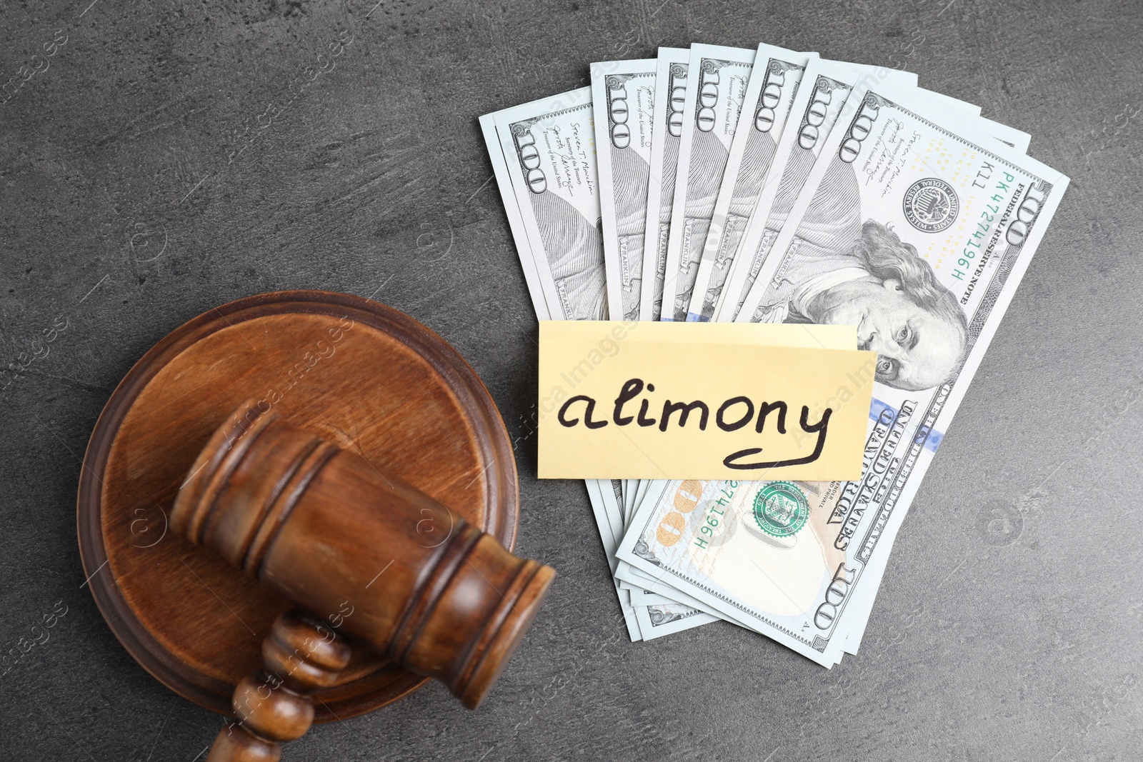 Photo of Card with word Alimony, dollar banknotes and wooden gavel on grey table, flat lay