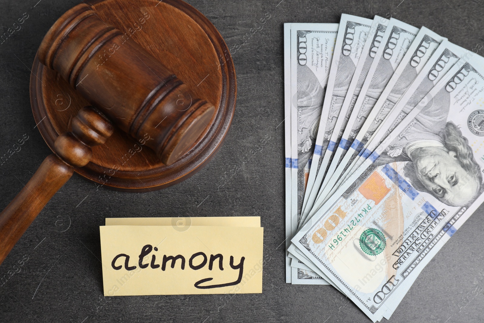 Photo of Card with word Alimony, dollar banknotes and wooden gavel on grey table, flat lay