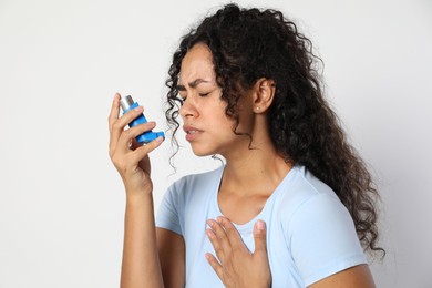 Young woman using asthma inhaler on white background